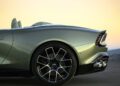 Rear side view of the world's fastest front-engined convertible, a sleek Aston Martin Vanquish, parked on a smooth surface. Its modern design stands out against the soft gradient sky background.
