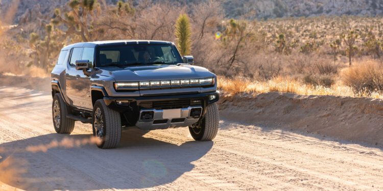 A Hummer EV SUV navigates a dusty desert road, searching for solace amidst the breathtaking mountainous landscape.