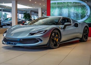 A sleek silver Hybrid V6 supercar with a low profile is parked indoors at a showroom, with a red and white wall behind it.