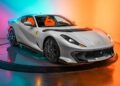 A silver Ferrari sports car with orange interior, part of our certified pre-owned Ferraris collection, is displayed on a rotating platform against a colorful orange and blue gradient background.