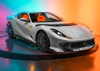 A silver Ferrari sports car with orange interior, part of our certified pre-owned Ferraris collection, is displayed on a rotating platform against a colorful orange and blue gradient background.