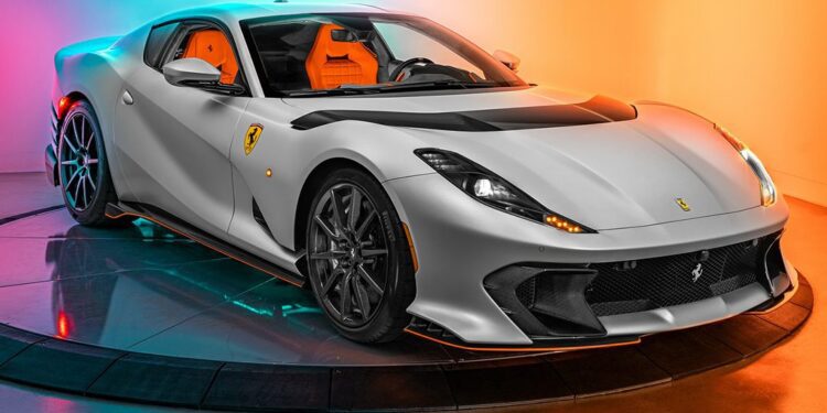 A silver Ferrari sports car with orange interior, part of our certified pre-owned Ferraris collection, is displayed on a rotating platform against a colorful orange and blue gradient background.