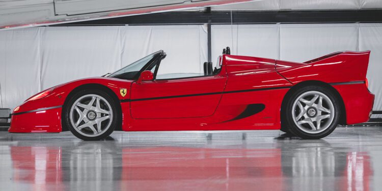 A sleek red Ferrari F50 sports car with a convertible top is parked indoors, featuring a shiny exterior and stylish rims, ready to dazzle at RM Sotheby's Miami auction and potentially set a world record price.