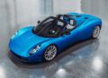 A sleek blue sports car with a convertible top on a reflective gray surface, featuring modern design and aerodynamic curves inspired by Goodwood's renowned automotive design.