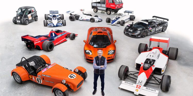 A person stands in front of a diverse lineup of vehicles, featuring race cars, a sports car, a microcar, and a small truck—each a testament to innovative automotive design—all displayed on a pristine white background.