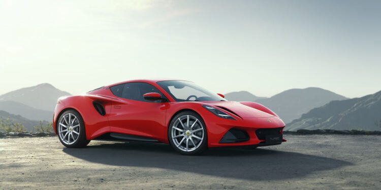 A sleek red sports car, the Lotus Emira Turbo, rests on a paved surface with majestic mountains in the backdrop under a clear sky, boasting an impressive 400HP.