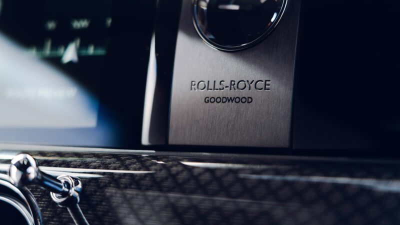 Close-up of a Rolls-Royce car interior, showing the embossed "Rolls-Royce Goodwood" logo on a metallic panel.