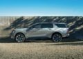 The sleek 2026 Escalade, a stunning silver SUV, is parked on gravel in front of a concrete wall, basking under a clear blue sky.