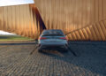 A sleek silver Audi RS 3, known for its powerful 5-cylinder engine, is parked on a cobblestone area in front of a modern copper-colored building with geometric lines.