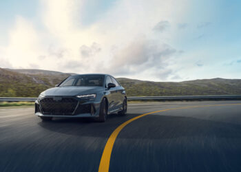 Under a cloudy sky, the sleek 2025 RS 3 confidently takes a sharp turn on a winding mountain road, showcasing Audi's impressive 5-cylinder legacy.