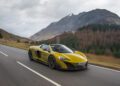 A yellow McLaren sports car gracefully navigates the scenic mountain road under overcast skies, capturing the thrill of the drive.