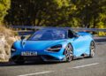 A sleek blue McLaren navigates a curved road flanked by lush trees, embodying the allure of LT Cars.