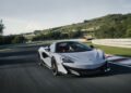 A sleek silver McLaren sports car expertly navigates the racetrack, with lush greenery and rolling hills as its backdrop.