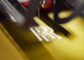Close-up of a sewing machine embroidering the opulent "RR" initials on yellow fabric, reminiscent of the craftsmanship found in a luxury Rolls-Royce.