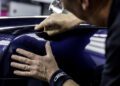 With precision and both hands, the person applies a protective film to the blue luxury car's surface, reminiscent of a Rolls-Royce build time dedication.