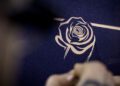 Close-up of a person etching an intricate rose design into a dark blue surface, reminiscent of the craftsmanship seen in luxury cars like Rolls-Royce.