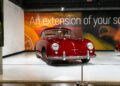A vintage red car is elegantly showcased in a showroom, beneath a large wall sign declaring "An extension of your soul." This exquisite exhibit is part of the ultra-exclusive lineup at the Porsche Experience Center.