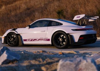 A sleek white 911 GT3 RS with a PTS Moongem finish flaunts its "GT3 RS" decal and large rear wing, resting on black wheels. It's parked stylishly on a dirt road, framed by dry grass, as if fresh from the Porsche Exchange showroom.