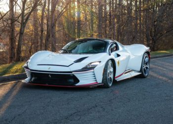A sleek white Ferrari sports car with red accents, reminiscent of the Daytona SP3, is parked on a paved road, surrounded by trees.