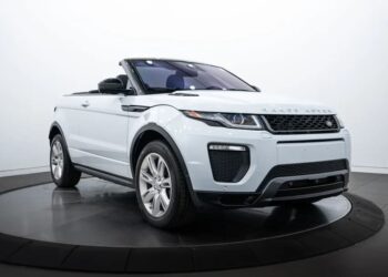 A white Range Rover Evoque convertible with its top down is displayed indoors on a rotating platform, showcasing the style and elegance of luxury cars.