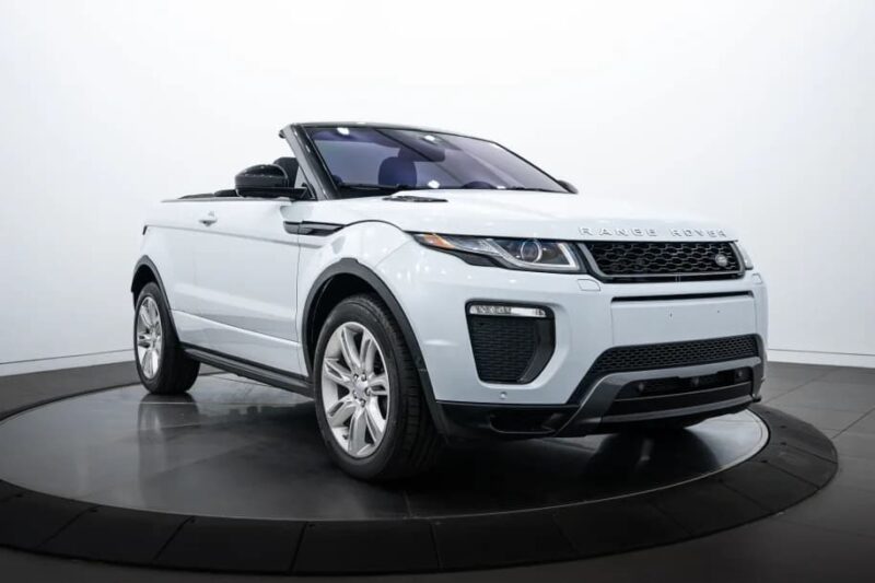 A white Range Rover Evoque convertible with its top down is displayed indoors on a rotating platform, showcasing the style and elegance of luxury cars.