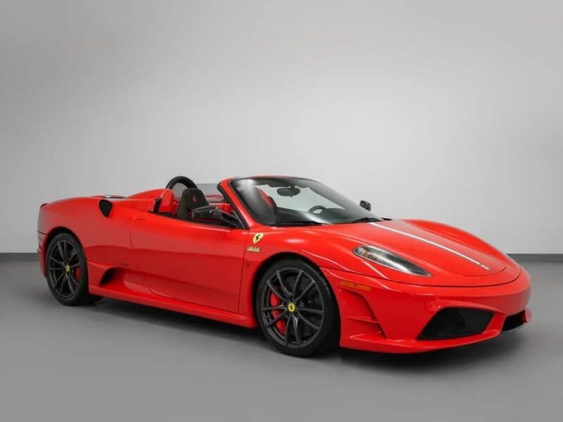 A red Ferrari 430 Scuderia convertible sports car with black wheels, featuring the iconic Prancing Horse emblem, is parked in a studio with a plain gray background and is now available for sale.