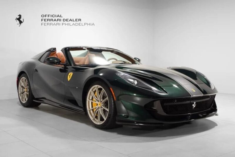 A dark green Ferrari sports car with gold wheels and a tan interior is displayed in a showroom with "Ferrari Philadelphia" branding on the wall, highlighting one of the best supercars for sale.