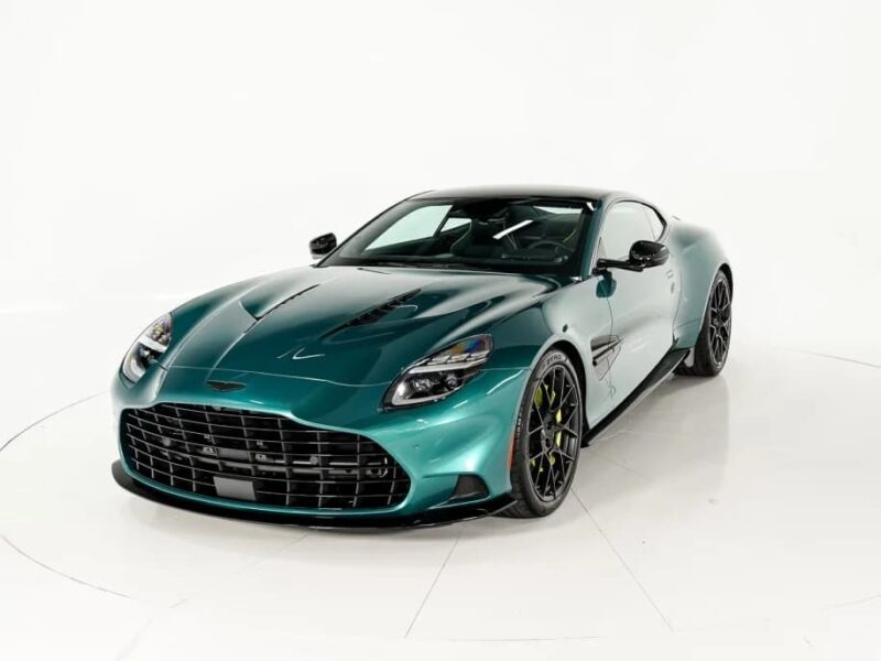 A green Aston Martin sports car, one of the best green supercars, is parked in a white studio setting, facing slightly left with visible black accents and yellow brake calipers.