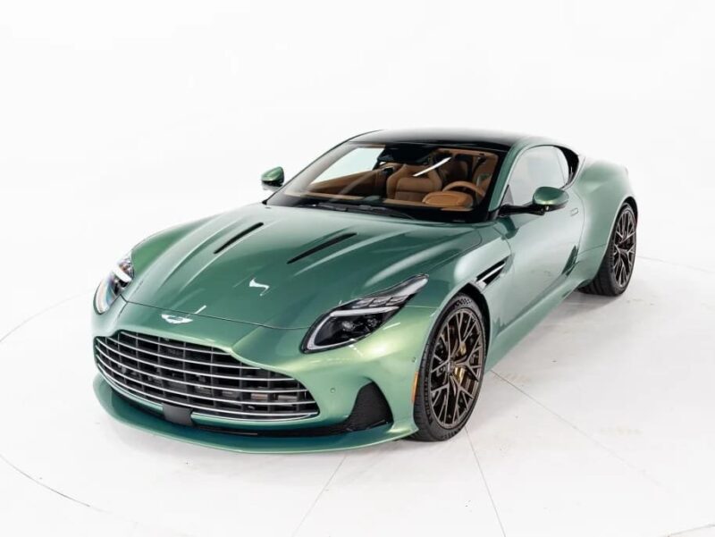 A green Aston Martin coupe, one of the best green supercars, is parked in a white studio, featuring a large front grille and brown leather interior.