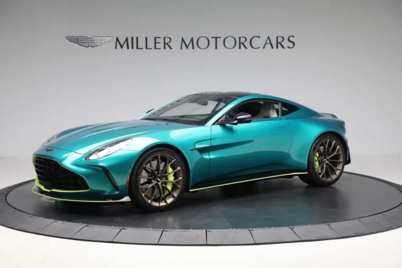 A teal Aston Martin coupe with black and lime green accents is displayed on a rotating platform in a showroom with "Miller Motorcars" branding, highlighting one of the best green supercars among exciting supercars for sale.