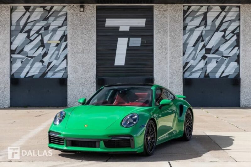A green Porsche sports car, one of the best supercars, is parked in front of a building with geometric-patterned garage doors and the letter "T" displayed.