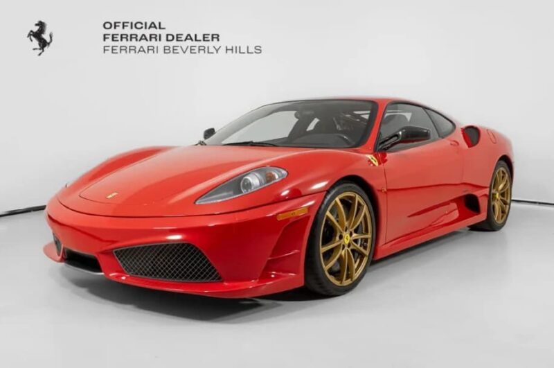 A red Ferrari 430 Scuderia sports car with gold wheels is displayed for sale in a showroom with a white background and Ferrari Beverly Hills signage.
