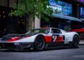 A sleek black and white Ford GT with red accents and the number "78" graces a city street, reflecting the urban architecture around it. Enhanced by Graham Rahal Performance, this LYNX Motors masterpiece stands poised next to a leafy tree.