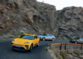 Three cars navigate one of Europe's Best Driving Roads, a winding mountain path lined with rocky cliffs. Leading the pack is a yellow Porsche Macan Turbo Electric, followed by a blue car and a black car as they take on the sharp curve to the right.