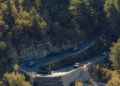 Four cars, including the sleek Macan Turbo, navigate a winding mountain road surrounded by dense forest.