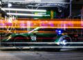At the brightly lit pit lane, team members hustle during a nighttime stop for racing car 120, against the backdrop of blurred light trails. The intensity echoes the spirit of the 12 Hours Of Sebring, with every second counting towards eventual victory.
