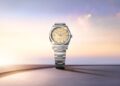 Displayed upright on a minimalist surface against a soft gradient sky background, this Rolex wristwatch features a silver case with a striking yellow dial and baton indices, embodying the elegance of the 2025 Watches collection presented at Watches & Wonders.