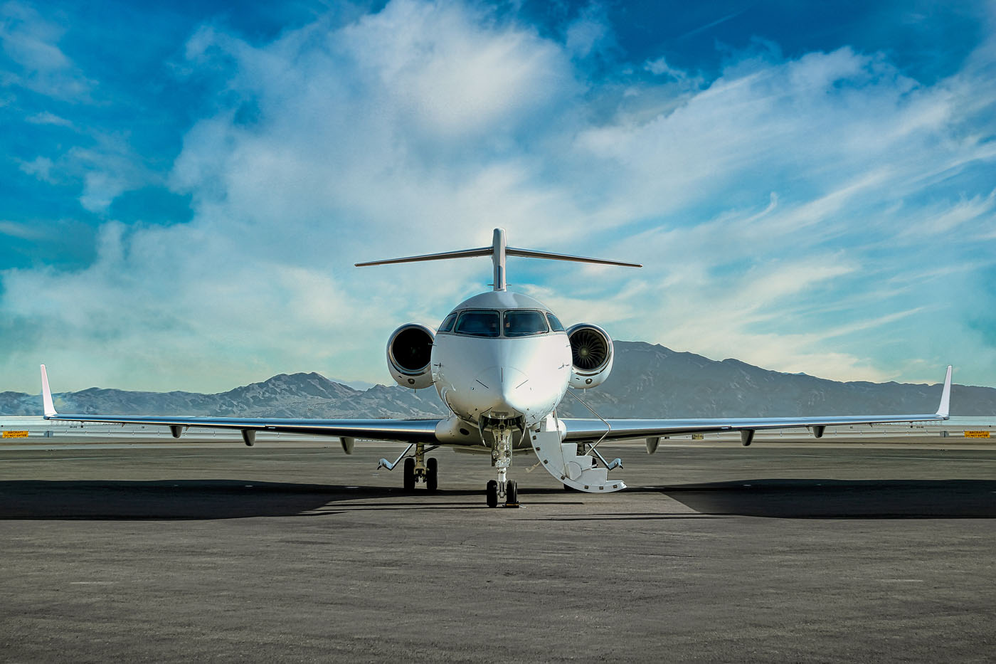 Jet pribadi putih dari jet bisnis Paramount duduk di landasan pacu, dibingkai oleh pegunungan yang megah dan langit yang sebagian berawan.