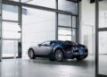 A blue and silver Bugatti Veyron sports car, featuring the iconic W16 engine, is parked inside a modern, glass-walled garage with large windows and minimalistic decor.