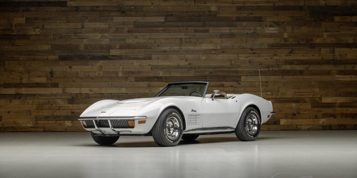 A white vintage convertible with the top down is parked indoors on a smooth floor, set against a wooden wall. The "Worldwide Auctioneers" logo hints at an Enthusiast Auction featuring a diverse lineup of classic cars.