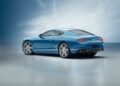 A blue Bentley Continental GT coupe car is elegantly parked on a reflective surface under a soft, cloudy sky.