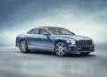 A sleek blue luxury Bentley sedan is parked on a smooth, reflective surface against a gradient blue background.