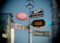 A street pole displays six whimsical signs—Gustaf Westman Park, Hot Wheels Boulevard, League of Legends Lane, Ice Spice St, KidSuper Ave—and is topped with a Mercedes-Benz CLA logo for a playful remix of pop culture influences.
