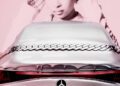 A metallic Mercedes-Benz CLA with a braided design on the trunk is parked in front of a large, monochrome portrait of a woman with curly hair, echoing the bold style of Ice Spice's latest remix.