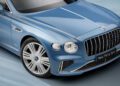 Close-up of a blue luxury sedan's front end, featuring a sleek grille, headlight, and chrome details. The license plate reads "New Flying Spur," showcasing the elegance synonymous with Bentley craftsmanship.