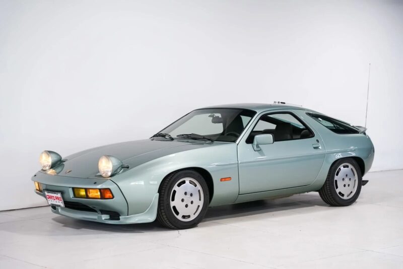 A silver Transaxle Porsche 928 sports car is parked in a white studio with its pop-up headlights raised—an inviting scene for those looking to invest in unsung classics.