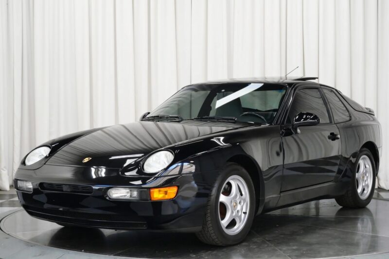 A black Porsche 968 transaxle sports car parked indoors with white curtains in the background—a true unsung classic and a smart choice for those looking to invest.