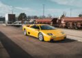 A rare Lamborghini Diablo VT 6.0, fresh from a Broad Arrow Auctions event, sits majestically on an industrial road near train tracks under a cloudy sky.
