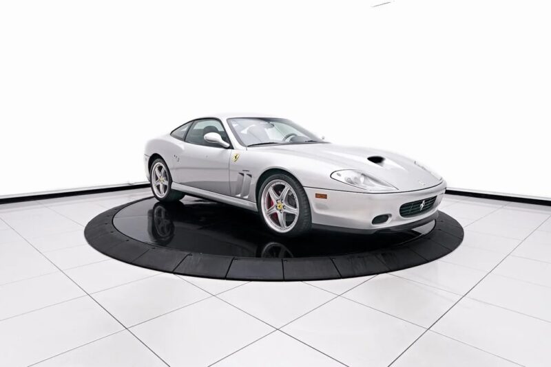 A Ferrari Silver Sports Car, which is celebrated among the best handcraft, is displayed on a circular black platform in a minimum white showroom.
