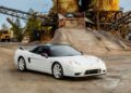 A sleek white Lamborghini Diablo rests in an industrial setting, surrounded by towering machinery and gravel piles.